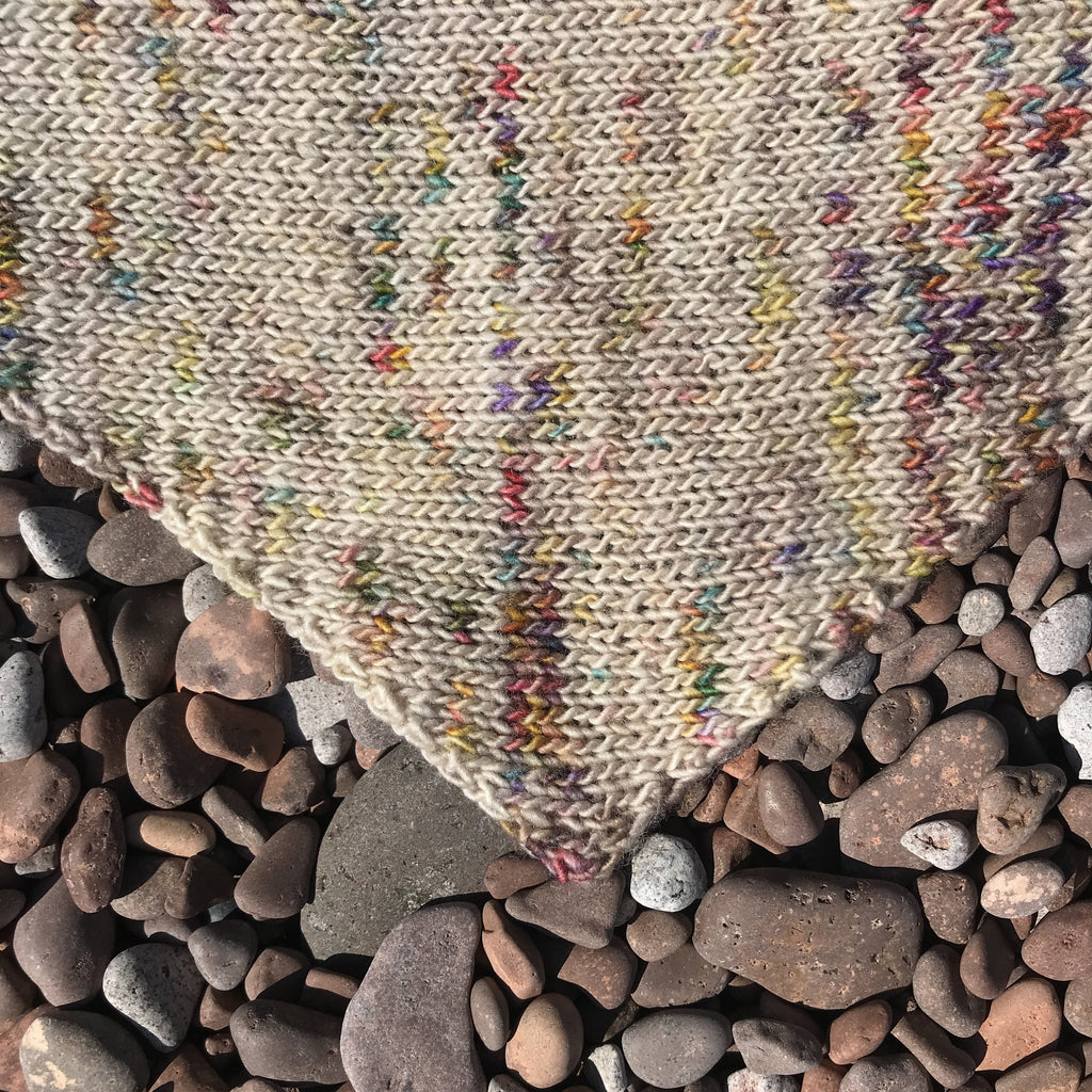 A close up shot of the Artist Point Scarf laying on a Minnesota beach shows the point at which the knitting pattern switches from increases to decreases. 